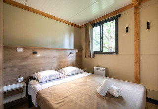 Interieur van Mobile home Vancouver chalet met dubbel bed, raam, houten panelen en sobere inrichting.