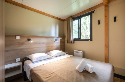 Interior of Mobile home Vancouver cabin featuring a double bed, window, wood paneling, and simple decor.