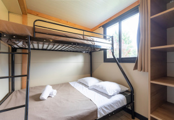 Zimmer im Mobile Home Vancouver mit Etagenbett, großem Fenster und offenen Regalen daneben.