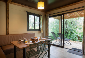 Comedor dentro del Chalet Ottawa en Huttopia Etang de Fouché, Francia, con vista a una terraza y vegetación.