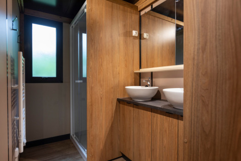 Baño moderno de madera con dos lavabos y espejo en Chalet Ottawa en Huttopia Etang de Fouché, Francia.