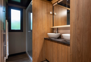 Modernes Badezimmer mit Holzverkleidung, zwei Waschbecken und Spiegel im Chalet Ottawa in Huttopia Etang de Fouché.