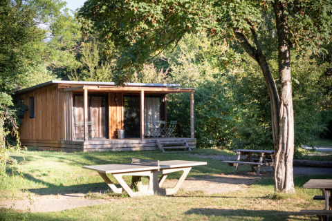 Træhytte kaldet Chalet Ottawa omgivet af grønne træer, med terrasse, picnicbord og betonbord udenfor.
