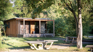 Houten hut Chalet Ottawa tussen het groen, met veranda, betonnen tafel en picknickbank op de voorgrond.
