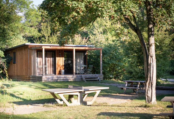 Houten hut Chalet Ottawa tussen het groen, met veranda, betonnen tafel en picknickbank op de voorgrond.