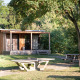 Træhytte kaldet Chalet Ottawa omgivet af grønne træer, med terrasse, picnicbord og betonbord udenfor.