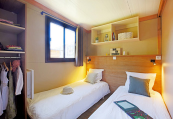 Dos camas individuales en un dormitorio luminoso del Chalet Ottawa, Huttopia Etang de Fouché, Francia, con armario abierto.