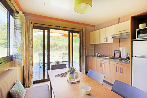Helles Wohnküchen-Interieur des Chalet Ottawa bei Huttopia Etang de Fouché in Frankreich mit Gartenblick.