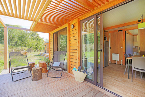 Helle Holzhütte mit überdachter Terrasse, Liegestühlen und Blick aufs Grüne bei Huttopia Etang de Fouché in Frankreich.