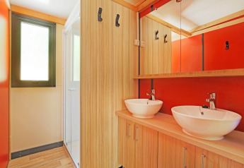 Moderne badkamer met dubbele wastafel, houten kasten en rode muren in Chalet Ottawa, Huttopia Etang de Fouché.