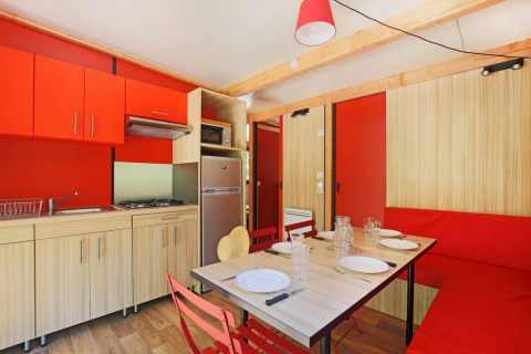 Küche und Essbereich im Chalet Ottawa bei Huttopia Etang de Fouché in Frankreich, mit roten und holzfarbenen Möbeln.
