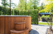 Udendørs vildmarksbad i træ med trappe ved Module Wood Hottub, Bospark Ede, Holland, omkranset af hæk.