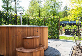 Holz-Whirlpool mit Treppe im Garten des Module Wood Hottub, Bospark Ede, Niederlande, mit grüner Hecke.