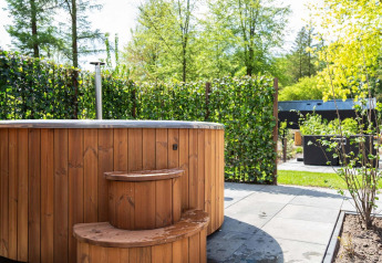 Udendørs vildmarksbad i træ med trappe ved Module Wood Hottub, Bospark Ede, Holland, omkranset af hæk.