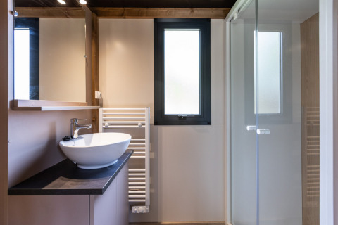 Modern bathroom at Chalet Victoria, Huttopia Gorges du Verdon, France, featuring sink, shower, and window.