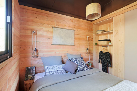 Knusse slaapkamer in een houten hut met tweepersoonsbed, open planken en moderne verlichting.