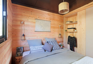 Dormitorio acogedor en una cabaña de madera con cama doble, estantes abiertos y lámparas modernas.