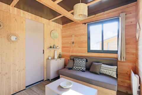 Stilfuldt interiør i Chalet Victoria på Huttopia Gorges du Verdon, Frankrig, med trævægge og moderne sofa.