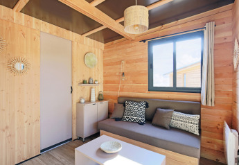 Stilfuldt interiør i Chalet Victoria på Huttopia Gorges du Verdon, Frankrig, med trævægge og moderne sofa.