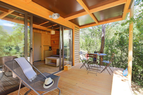 Terraza de madera con sillas y mesa en Chalet Victoria, Huttopia Gorges du Verdon, Francia, rodeada de naturaleza.