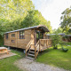Træbeklædt Gypsy caravan lodge med veranda og picnicbord i grøn, frodig natur om sommeren.