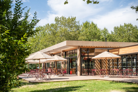 Terraza al aire libre con sombrillas y mesas en Camping de Paris, rodeada de vegetación exuberante.