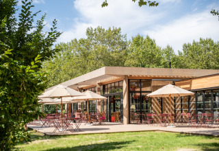 Outdoor café terrace with umbrellas and seating at Camping de Paris, surrounded by lush greenery.