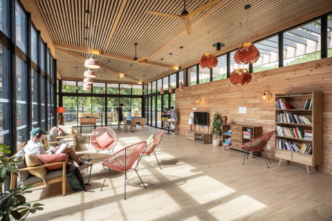 Sala luminosa con muebles de madera, ventanales y personas relajándose en Camping de Paris, Île de France.