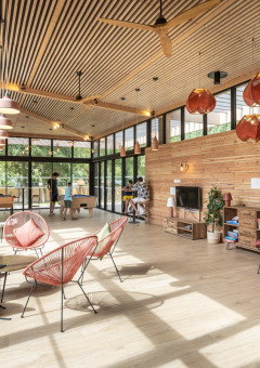 Sala luminosa con muebles de madera, ventanales y personas relajándose en Camping de Paris, Île de France.