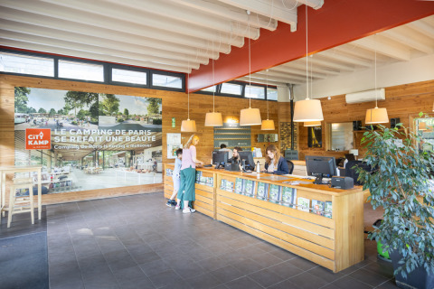 Camping de Paris reception area with guests speaking to staff at the front desk, Île de France, France.
