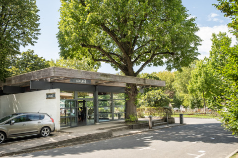 Entrada al Camping de Paris en Île de France, con coche, edificio moderno y frondosos árboles verdes.