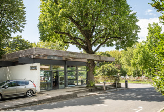 Indgang til Camping de Paris feriepark i Île de France med bil, moderne bygning og grønne træer.