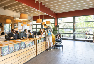 Reception area at Camping de Paris, Île de France, France, with staff assisting guests and a family with a stroller.