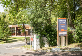 Indgang til Camping de Paris i Île de France, Frankrig, et feriepark omgivet af grønne træer og natur.