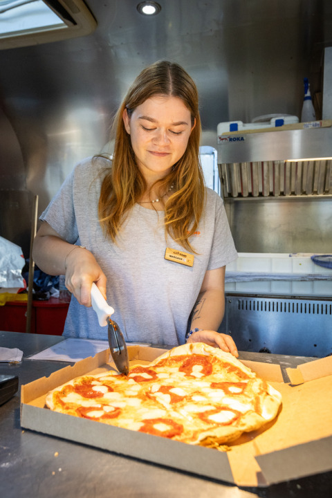 Mujer cortando pizza con un cortador en la cocina del Camping de Paris, parque vacacional en Île de France, Francia.