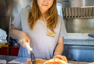 Frau schneidet Pizza mit einem Pizzaschneider im Camping de Paris, Ferienpark in Île de France, Frankreich.