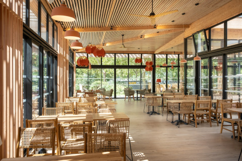 Luminoso comedor con muebles de madera y grandes ventanales en Camping de Paris, Île de France, Francia.
