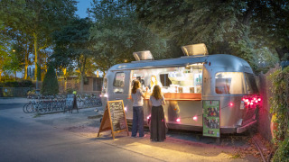 Avondopname van een foodtruck op Camping de Paris, Île de France, Frankrijk, met klanten bij het raam.