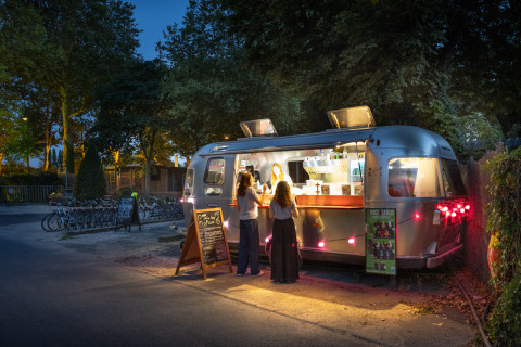 Streetfood-Wagen bei Nacht im Camping de Paris in Île de France, Frankreich, mit Kunden davor.