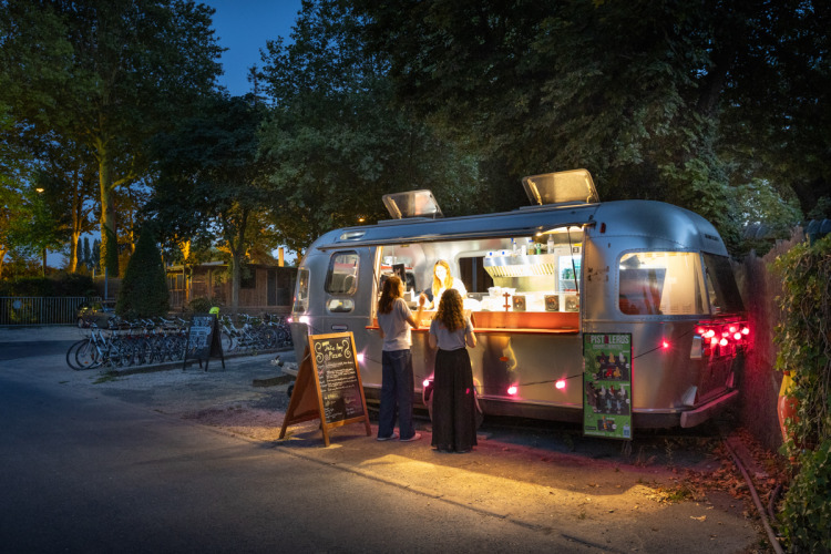 Vue nocturne d’un food truck au Camping de Paris, Île de France, France, servant des clients dehors.