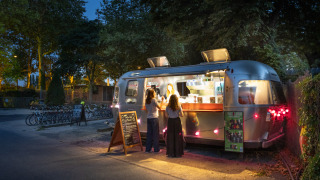 Caravana de comida ubicada en Camping de Paris, Île de France, Francia, con clientes durante la noche.