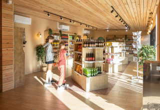 Indkøbsscene i den lyse butik på Camping de Paris, med to personer, hylder og naturlig belysning.