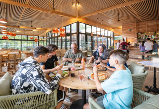 Familie nyder pizza sammen inde i en moderne restaurant på Camping de Paris, Île de France, Frankrig.
