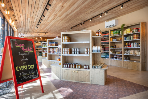 Supermarkt im Camping de Paris, Île de France – helle Holzregale, Produkte und eine Kreidetafel.