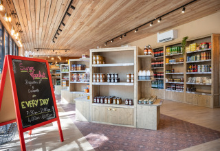 Supermarkt im Camping de Paris, Île de France – helle Holzregale, Produkte und eine Kreidetafel.