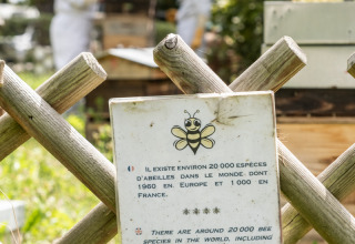 Informationsskilt om bier ved biavlerområde i Camping de Paris, Île de France, med to personer i biavlertøj.