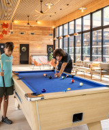 Des enfants jouent au billard dans un espace commun lumineux au Camping de Paris, en Île de France.