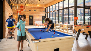 Kinderen spelen biljart in een lichte lounge van Camping de Paris, een vakantiepark in Île de France.