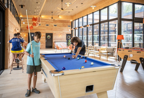 Børn hygger sig med billard i et lyst fællesområde på Camping de Paris, feriepark i Île de France.