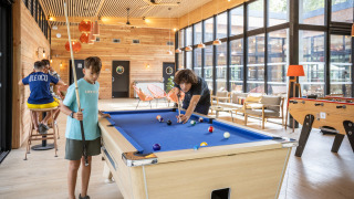 Niños juegan al billar en una sala luminosa de Camping de Paris, un parque vacacional en Île de France.